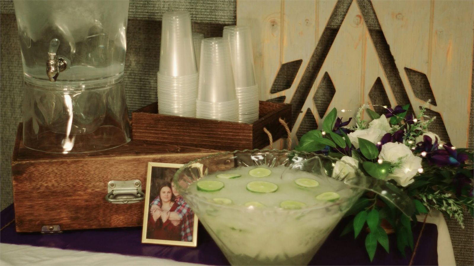 Rustic drink station with a glass dispenser, punch bowl and floral arrangement