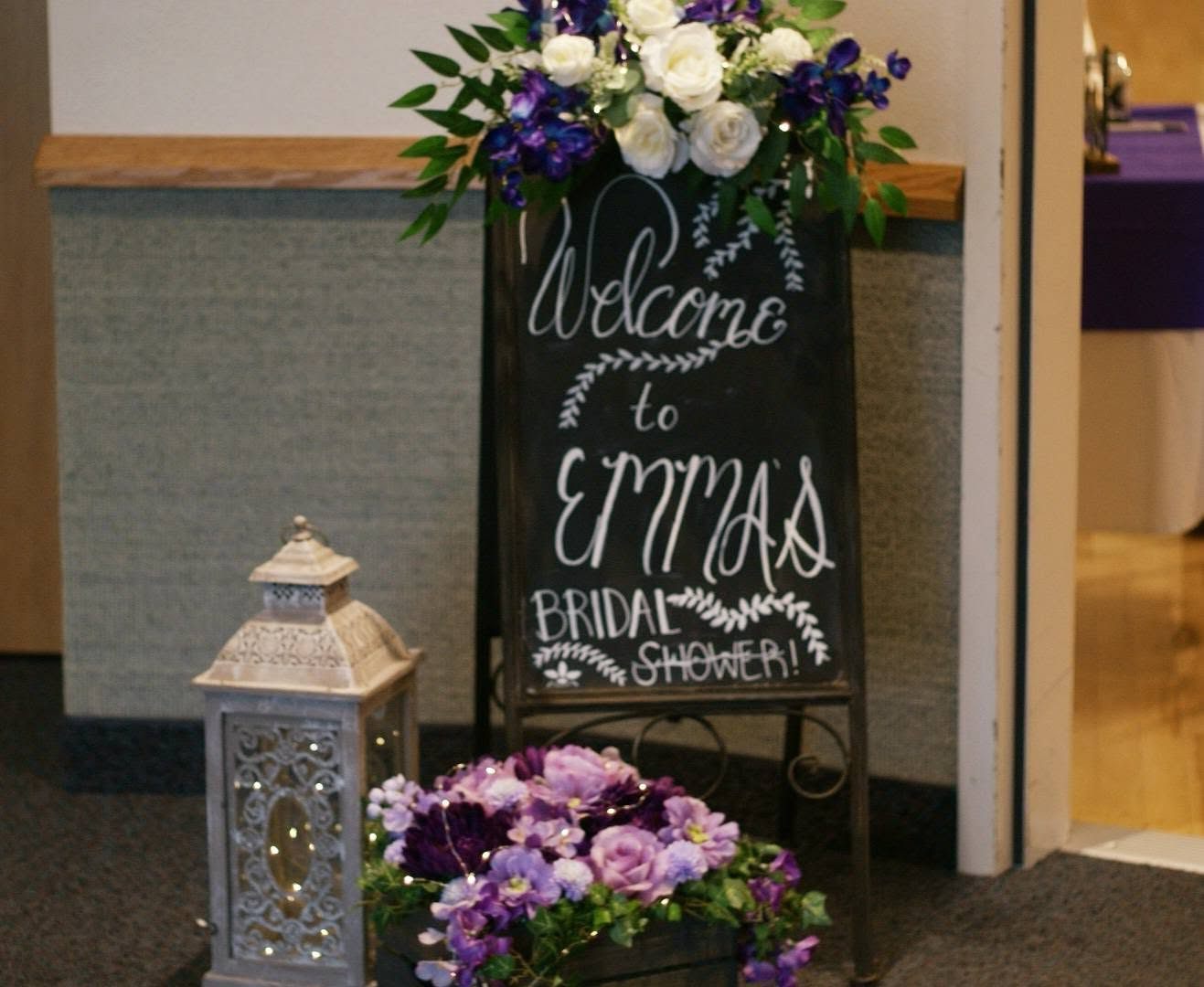 Hand lettered chalkboard welcome sign with floral swag and lantern